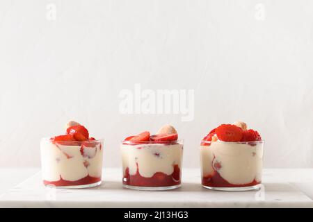 Trois portions de dessert de trifle en pots de verre avec biscuit savoyardi, fromage mascarpone décoré de fraises sur fond blanc. Banque D'Images