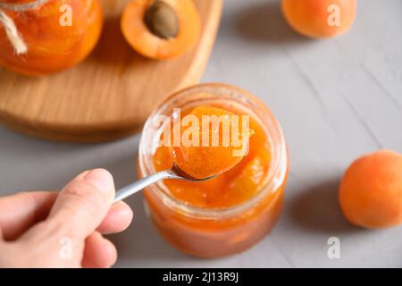 Goûtez la confiture d'abricot dans un pot en verre sur fond gris. Récolte d'été et conserves. Gros plan. Banque D'Images