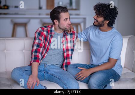 Couple gay biracial ayant une conversation sur le canapé Banque D'Images