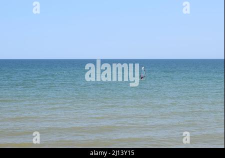 L'homme est engagé dans la planche à voile sur fond bleu de mer et de ciel. L'homme monte à bord avec une voile. Planche à voile sur des eaux calmes. Azov Banque D'Images