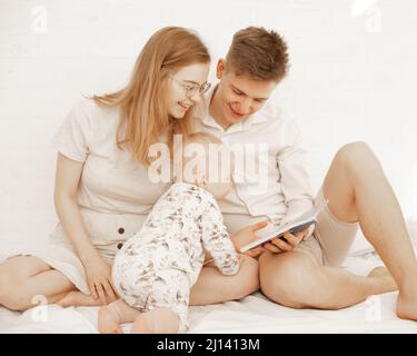 Heureux famille passer du temps ensemble, pieds nus mère, père, bébé. Livre de lecture conte de fées, décrire dans la chambre de linge de maison Banque D'Images