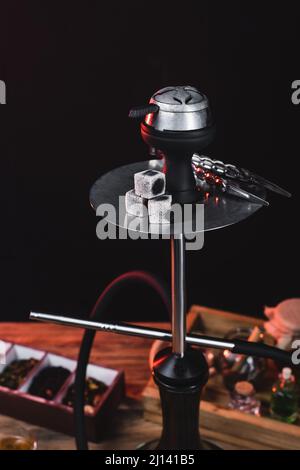 Narguilé avec des charbons près du thé sec flou isolé sur le noir Banque D'Images