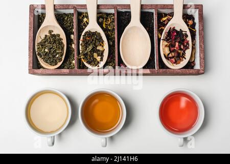 Vue de dessus du thé dans les tasses près des cuillères en bois et de la boîte sur fond blanc Banque D'Images