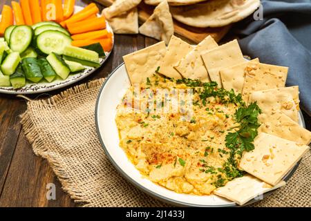 Vue imprenable sur un bol avec houmous maison avec pain pita et craquelins et dans un autre bol carottes et autres légumes. Concept de frais, sain et Banque D'Images