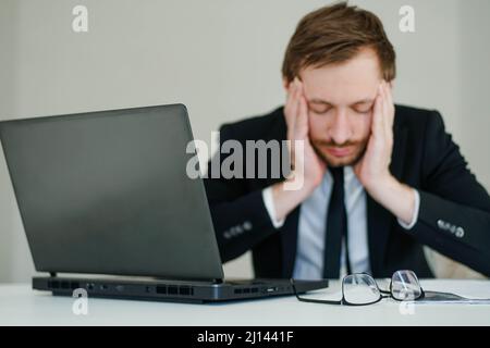 Agacé jeune homme d'affaires en costume travaillant sur un ordinateur portable et massage de la tête sentir la douleur migraine, stressé. Banque D'Images