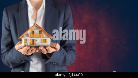 Section médiane d'une femme agent immobilier tenant un modèle de maison contre l'espace de copie sur fond rouge Banque D'Images