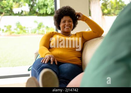 Portrait complet d'une femme mi-adulte afro-américaine souriante assise sur un canapé à la maison Banque D'Images