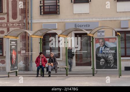 Mosonmagyarovar, Hongrie. 18th mars 2022. Un couple attend un arrêt de bus avec un panneau d'affichage des élections pour le Premier ministre hongrois Viktor Orban du parti Fidesz dans la rue. Mosonmagyarovar est la ville du nord-ouest de la Hongrie située à environ 160 kilomètres de la capitale hongroise Budapest. Peter Marki-Zay défiera le Premier ministre Viktor Orban lors des prochaines élections législatives, qui auront lieu le 3rd avril 2022. (Photo de Tomas Tkachik/SOPA Images/Sipa USA) crédit: SIPA USA/Alay Live News Banque D'Images