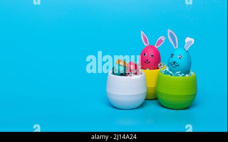 Dans un pot vert et blanc, les œufs de Pâques avec oreilles de lièvre se trouvent sur un fond bleu Banque D'Images