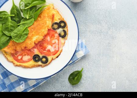 Omelette aux tomates, olives noires, fromage cottage et herbes aux épinards verts sur plaque blanche sur fond de béton gris. Délicieux petit déjeuner. En bonne santé Banque D'Images