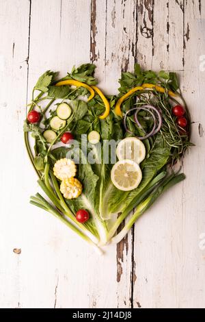 Vue en hauteur des légumes frais verts disposés en forme de coeur sur une table en bois blanc Banque D'Images