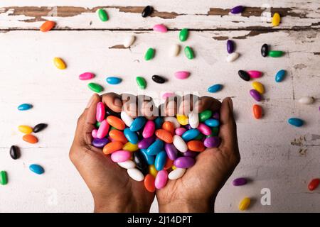 Directement au-dessus de la vue des mains coupées tenant des bonbons multicolores en forme de coeur sur une table en bois Banque D'Images