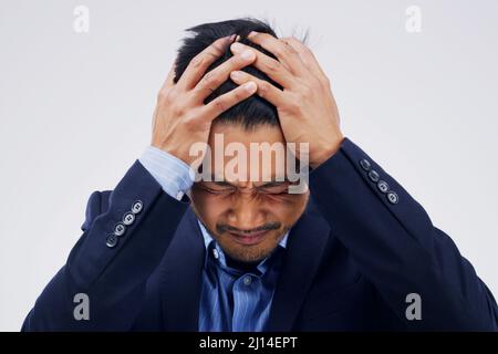 Ma tête a l'impression d'exploser. Prise de vue d'un jeune homme tenant sa tête tout en souffrant d'un mal de tête sur fond gris. Banque D'Images