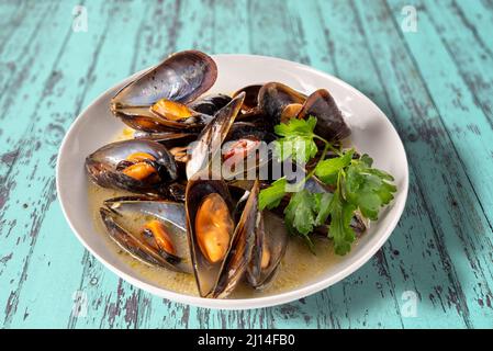 Moules cuites avec une recette italienne appelée moules tarantina en blanc, dans une assiette avec persil sur une table en bois bleu rustique Banque D'Images