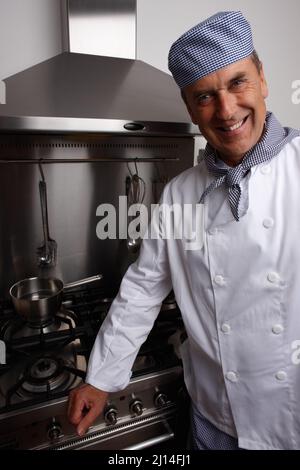 Chef cuisinier souriant debout près d'un poêle à gaz et d'une hotte. Portrait d'un chef senior souriant debout près d'un poêle à gaz et d'une hotte. Banque D'Images