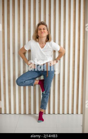 Portrait complet de femme blonde amusante. Une femme se tenant près d'un mur et fait des visages sur la caméra Banque D'Images