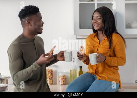 Loisirs pour couple. Happy Black conjoints boire du café avec des biscuits dans la cuisine confortable Banque D'Images