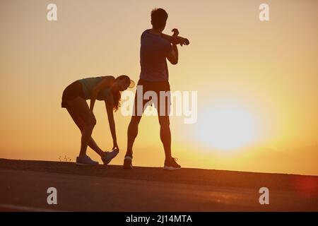 Sentir la brûlure et l'aimer. Photo d'un couple silhoueté pour une course au lever du soleil. Banque D'Images