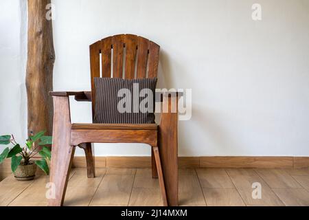 chaise en bois avec oreiller rayé sur un sol en bois contre un mur blanc. Maison à côté de la chaise Banque D'Images