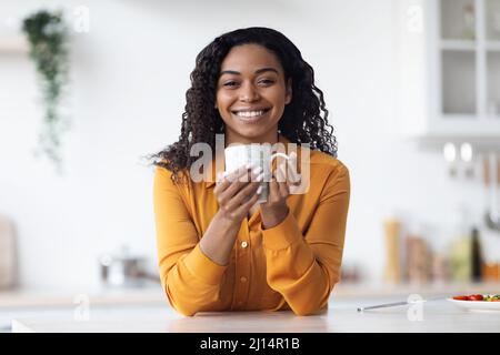 Une femme afro-américaine joyeuse qui boit du thé à la maison Banque D'Images