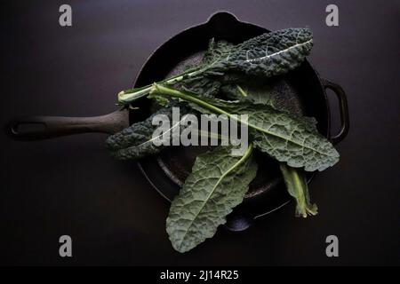 Kale non coupée dans une poêle en fonte sur fond noir Banque D'Images