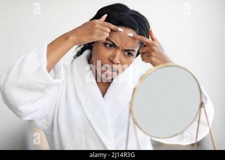 Jeune femme noire debout devant le miroir, en enlevant les têtes noires Banque D'Images