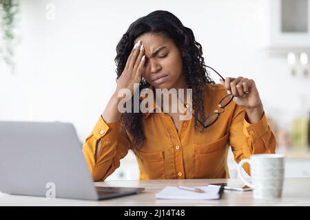 Femme noire épuisée souffrant de maux de tête lorsqu'elle travaille à domicile Banque D'Images