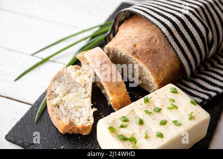 Bon pain de farine de blé maison fraîchement cuit avec beurre et bloc de beurre à côté sur la plaque de service en pierre noire dans la cuisine maison. Banque D'Images