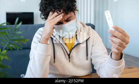 Un homme caucasien triste fait un appareil de test rapide à domicile pour Covid19 virus avec un résultat positif et tenant sa tête à la main à la table en bois. antigène actif Banque D'Images