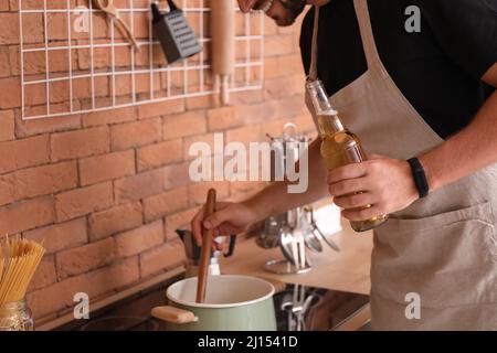 Beau homme buvant de la bière tout en cuisinant dans la cuisine Banque D'Images