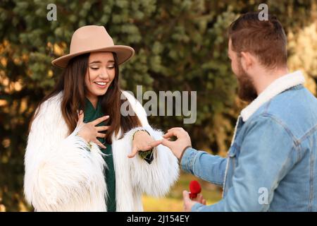 Jeune homme mettant l'anneau sur le doigt de son fiancé après la proposition de mariage dans le parc Banque D'Images