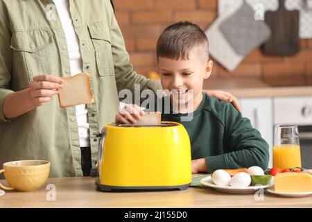 Petit garçon et sa mère mettant des tranches de pain dans le grille-pain dans la cuisine Banque D'Images