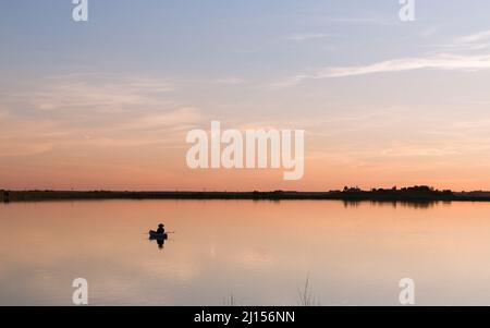 Pêcheur flottant sur le lac STILL au coucher du soleil Banque D'Images