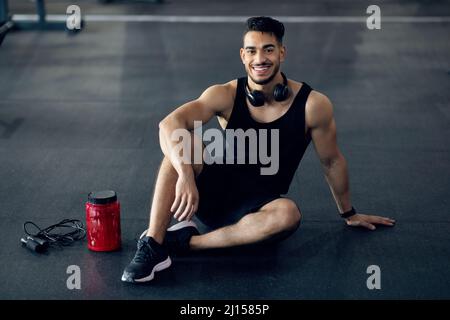 Beau athlète arabe masculin se détendant sur le sol à la salle de gym après l'entraînement Banque D'Images