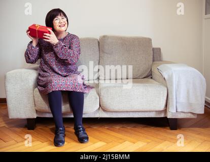 Grand-mère reçoit un cadeau sur son canapé gris à la maison horizontale Banque D'Images