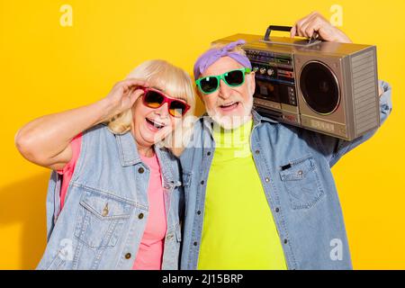 Photo de mignon excité mari femme porter jeans chemises sombre lunettes écoute boombox isolé couleur jaune fond Banque D'Images