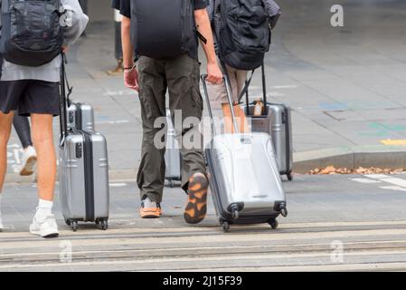 Quatre jeunes (de derrière, pas de visages) traversant une route à Sydney, en Australie, tirant des bagages à roulettes ou en ligne Banque D'Images