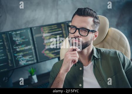 Photo d'un jeune homme intelligent et réfléchi habillé kaki chemise lunettes bras menton projetant un nouveau design de jeu à l'intérieur poste de travail Banque D'Images