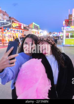 Deux amis plaisantant en prenant un selfie tenant un bonbon de coton dans une foire de nuit Banque D'Images