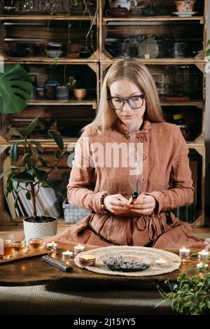 Femme méditant avec palo santo en studio, espace de nettoyage avec de la fumée. Personne adulte utilisant des incenses spirituelles brûlantes à la maison Banque D'Images