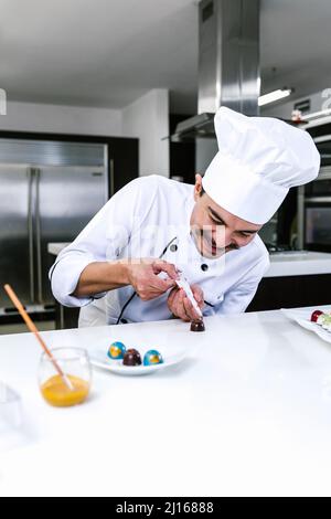 Jeune latiman chocolatier en chapeau de chef, avec bonbons mexicains au chocolat sur une assiette dans une cuisine commerciale au Mexique Amérique latine Banque D'Images