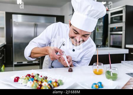 Jeune latiman chocolatier en chapeau de chef, avec bonbons mexicains au chocolat sur une assiette dans une cuisine commerciale au Mexique Amérique latine Banque D'Images