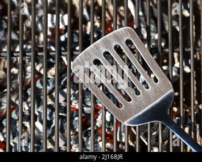 spatule en acier inoxydable sur grille de barbecue vide sur charbon de bois brillant, vue de dessus Banque D'Images