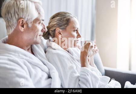 Quel super jour pour se détendre. Photo d'un couple joyeux d'âge moyen se relaxant ensemble tout en portant des peignoirs et assis sur un canapé à l'intérieur d'un spa Banque D'Images