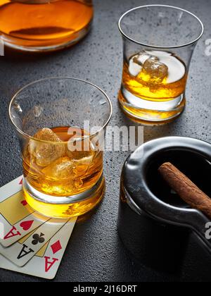 Deux verres de whisky avec glace, cigare dans un cendrier et cartes de poker. Jeu de poker, cigare et whisky concept. Banque D'Images