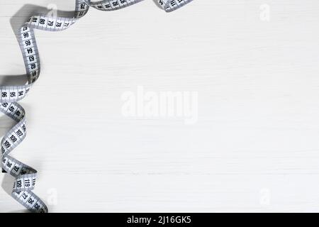 Mètre à ruban blanc déplié, ruban de mesure blanc isolé sur fond en bois blanc. Gros plan d'un mètre ruban sur un fond blanc. Le Banque D'Images