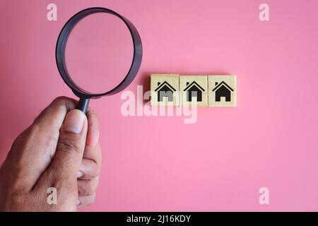 Recherche, concept de maison d'inspection. Main tenant la loupe et les cubes en bois avec icône de maison Banque D'Images