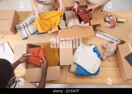 De la vue ci-dessus photo de volontaires non reconnaissables emballant des vêtements dans des boîtes en carton pour le don Banque D'Images