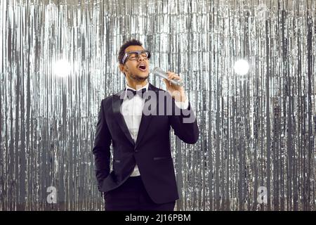 Jeune chanteur noir en costume de tuxedo debout sur scène, tenant le microphone et le chant Banque D'Images