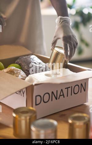 Homme afro-américain méconnu portant des gants de protection en latex emballant les fournitures alimentaires dans la boîte de dons Banque D'Images